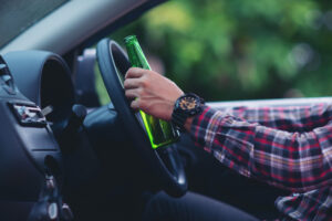 Mężczyzna trzymający butelkę piwa za kierownicą samochodu – konsekwencje prawne i obrona w sprawach o jazdę pod wpływem alkoholu.
